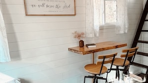 A cozy room with a wooden table and chairs, a bench, a window with curtains, and a framed quote on the wall.