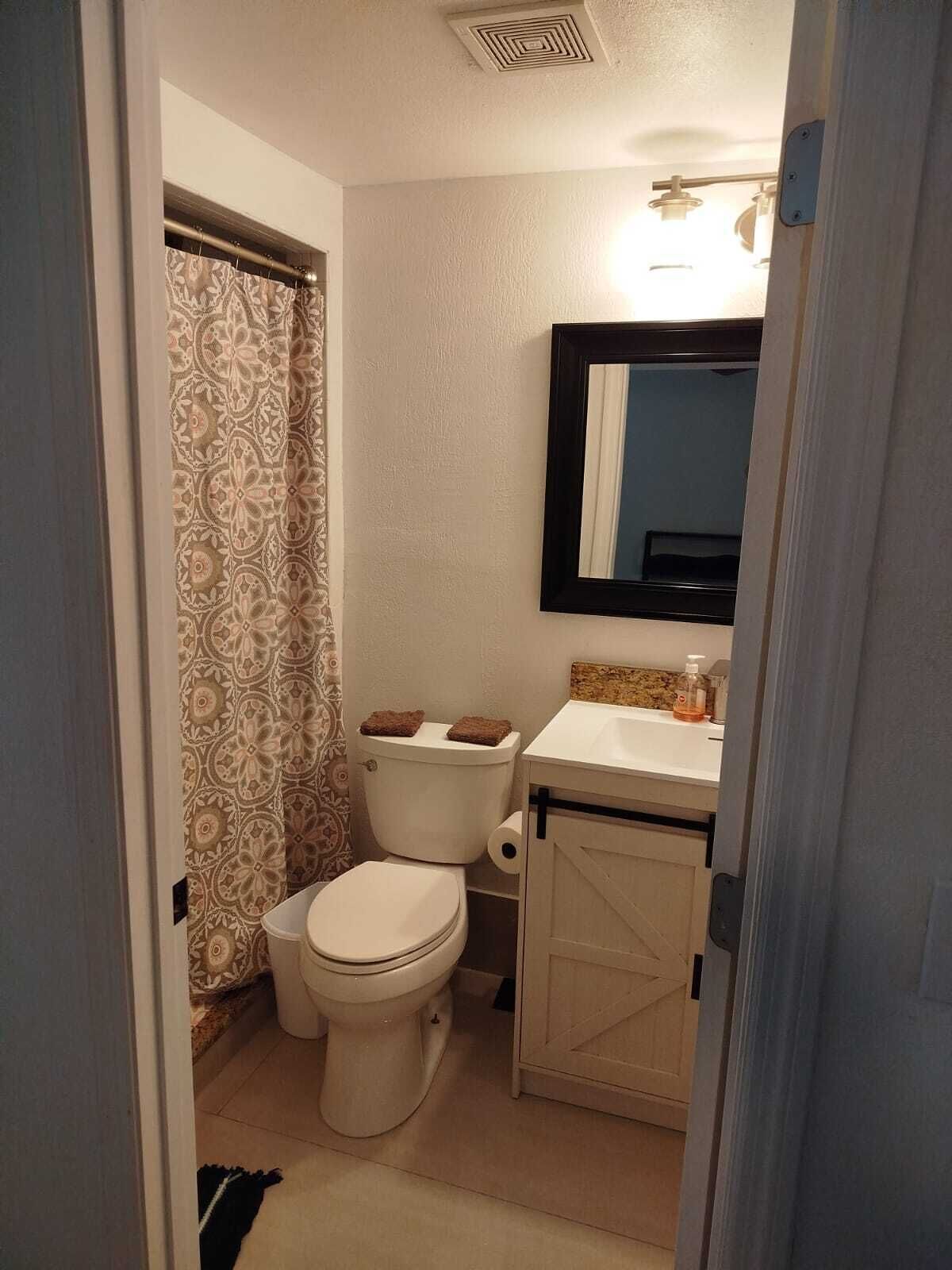 Et lille badeværelse med toilet, håndvask og bruseforhæng.