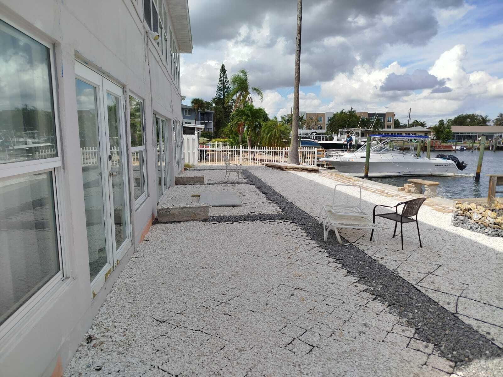 A patio area with a white building, a white fence, a boat dock, and a calm water body.