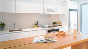 A modern kitchen with white cabinets, a stainless steel sink, a microwave, and a built-in oven. There's a wooden countertop with a book, a bottle of wine, and a loaf of bread. - Beach Haus Key Biscayne II (Key Biscayne)