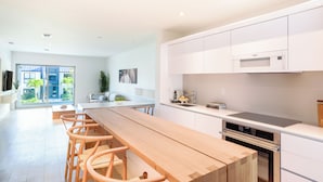 A modern kitchen with white cabinets, a wooden dining table, and a built-in oven. - Beach Haus Key Biscayne II (Key Biscayne)