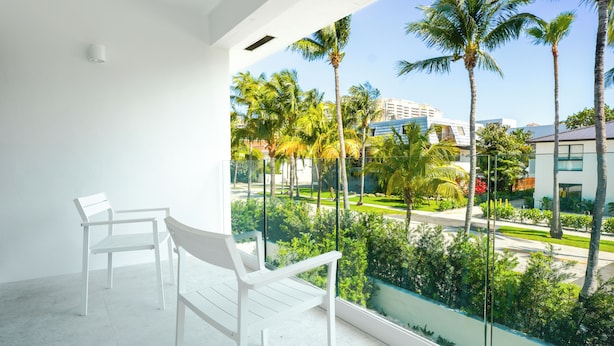 A balcony with white chairs and a view of palm trees and buildings. - Beach Haus Key Biscayne II (Key Biscayne)