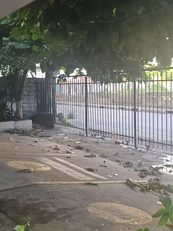 Un área cercada con superficie de concreto y algunos escombros dispersos, delimitada por una valla metálica.