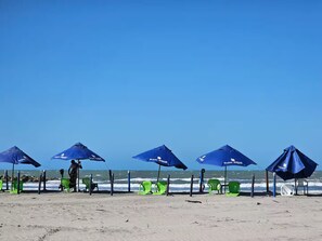 Una playa con múltiples sombrillas azules y sillas de plástico verde.