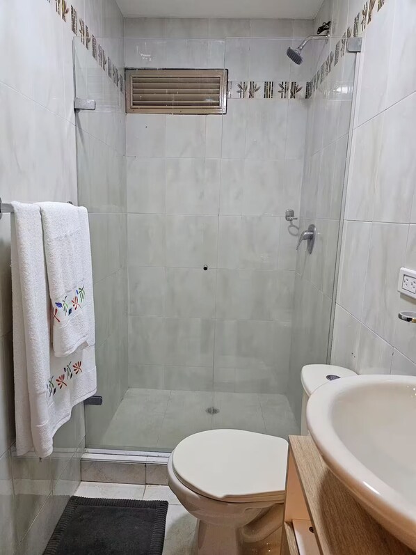 A modern bathroom with a glass shower enclosure, a toilet, and a freestanding bathtub.