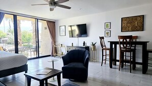A modern hotel room with a large bed, a seating area with a chair and table, a balcony with a view, and a flat-screen TV mounted on the wall. - Palm Desert Studio at Shadow Mountain Resort...steps to El Paseo`s Charms (Palm Desert)