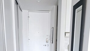 A hallway with a white door at the end, light grey tiled flooring, and a large mirror on the right wall. - Palm Desert Studio at Shadow Mountain Resort...steps to El Paseo`s Charms (Palm Desert)