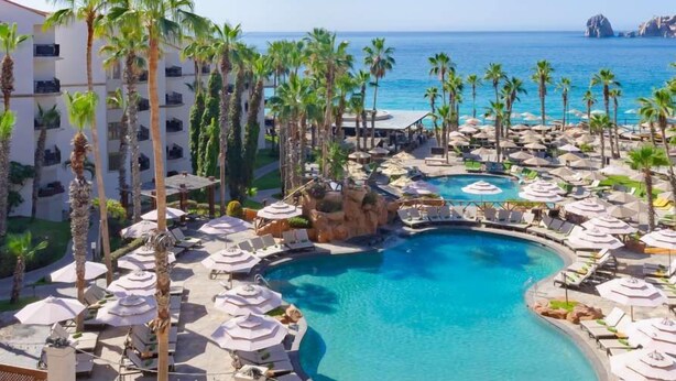 Un resort con una grande piscina, palme e vista sull'oceano.
