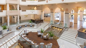 Un ampio atrio con diversi livelli, una zona salotto centrale con arredamento moderno e un elemento decorativo acquatico.