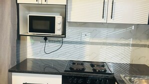 Une cuisine de taille réduite avec des meubles blancs, une cuisinière noire, un four à micro-ondes et un évier.