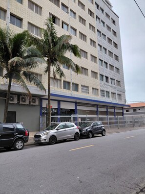 A multi-story building with a patterned facade, parked cars, and a palm tree in the foreground.