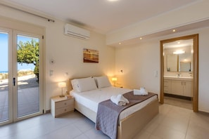 Habitación de hotel con cama, mesitas de noche, aire acondicionado, un cuadro, baño con espejo y puerta.