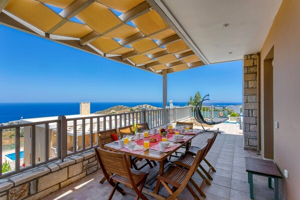 Un área de comedor exterior cubierta con una mesa dispuesta para cuatro personas, con vistas panorámicas al mar.