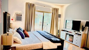 Ein Schlafzimmer mit einem Bett, Vorhängen, einem Fernseher, einer Lampe und einem kleinen Tisch.