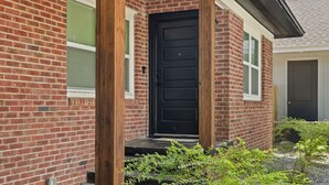 A brick house with a black front door, a small porch, and a window with a green shutter.