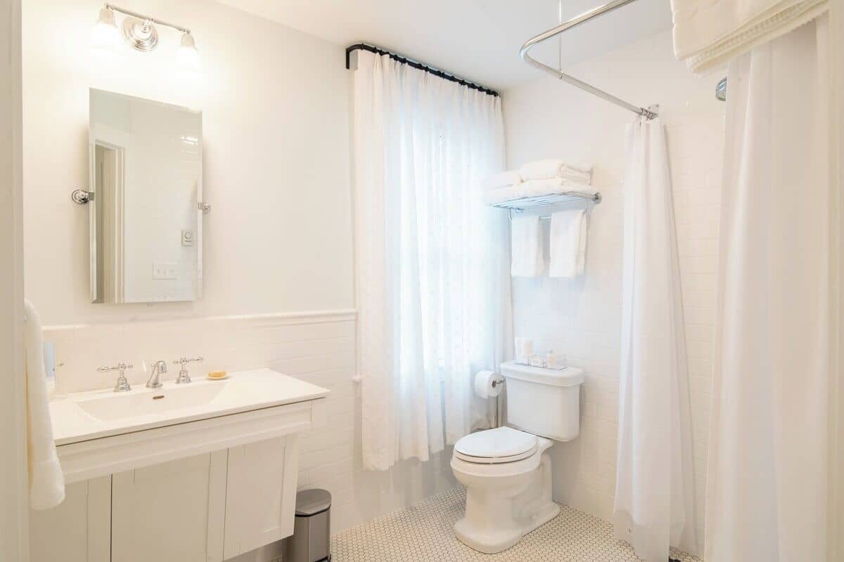 A modern bathroom with a white sink, mirror, toilet, and shower curtain.