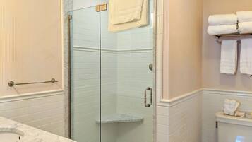 A bathroom with a glass shower enclosure, a marble sink, and a towel rack with folded towels.