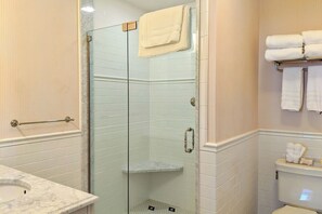 A bathroom with a glass shower enclosure, a marble sink, and a towel rack with folded towels.