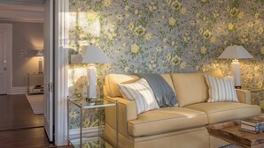 A living room with a beige sofa, two lamps, and a floral wallpaper. - Margin Street Inn (Westerly)