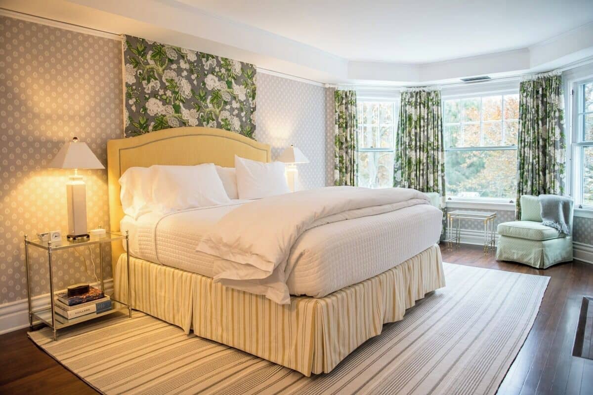 A bedroom with a large bed, two bedside tables, a chair, and a window with curtains.