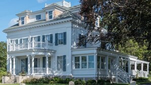 A large, white, two-story house with a balcony and a covered porch. - Margin Street Inn (Westerly)