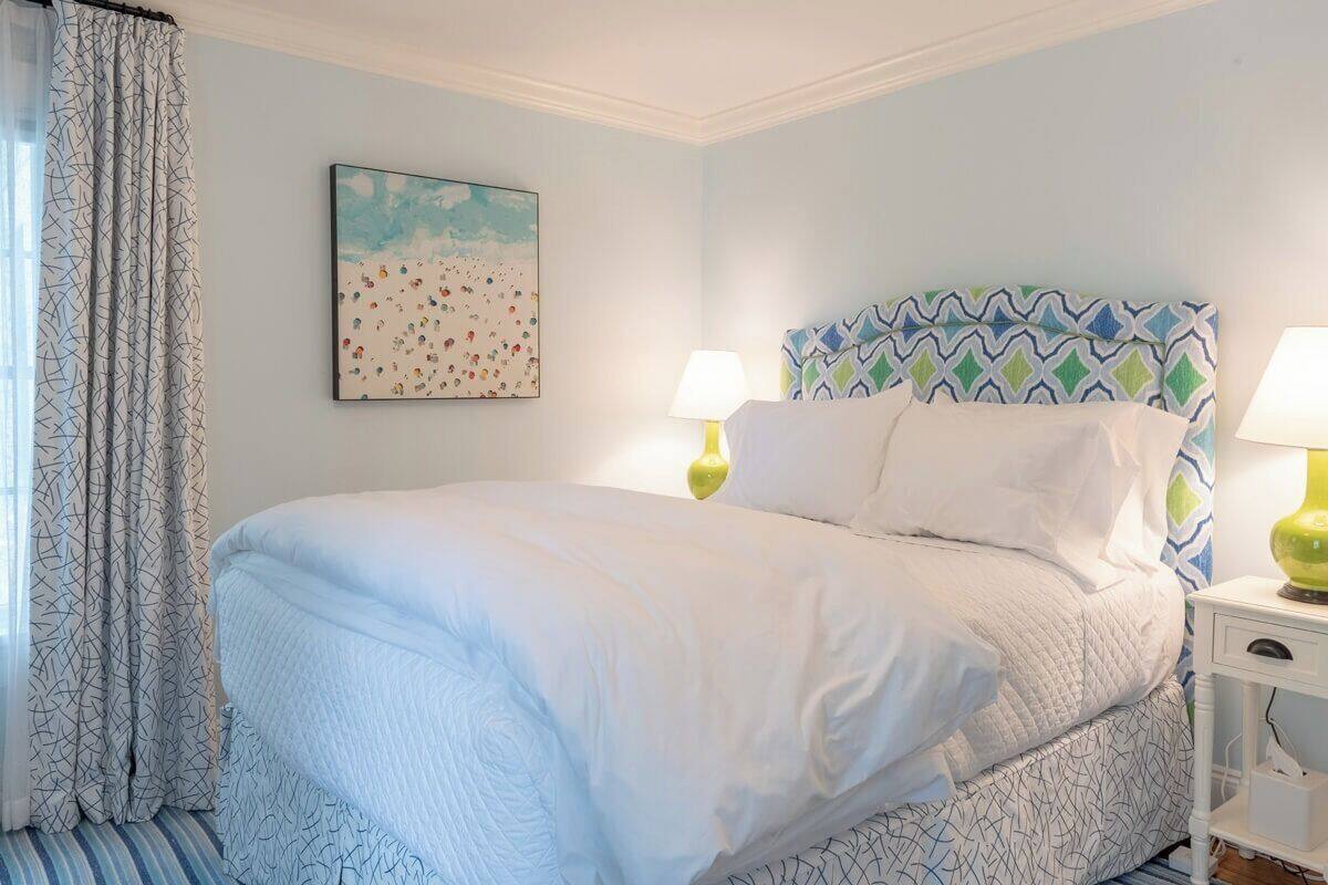 A neatly made bed with a patterned headboard, a bedside table with a lamp, and a wall painting.