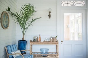 A room with a wicker chair, a large potted plant, a small table with a blue glass bowl, and a white door with a window. - Margin Street Inn (Westerly)