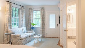 A bedroom with a bed, a sofa, a small table, and a window with curtains. - Margin Street Inn (Westerly)