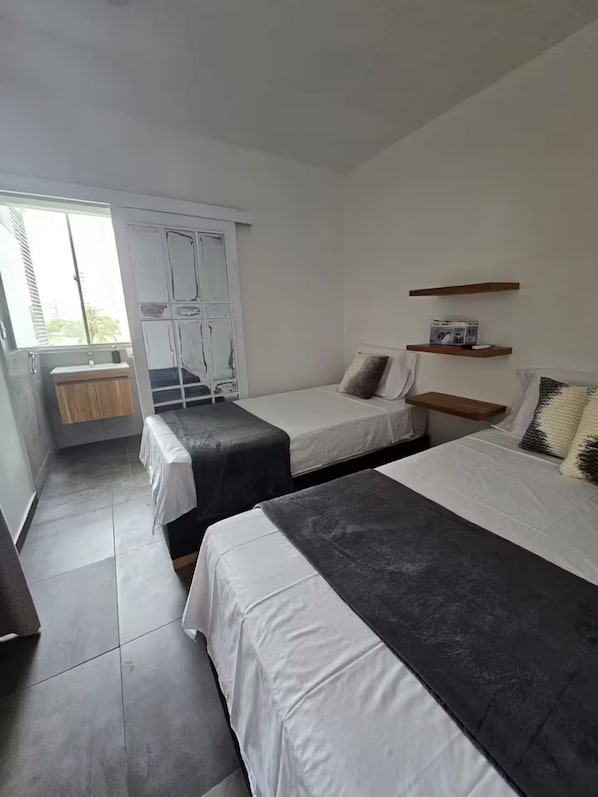 A modern bedroom with two beds, a window, a wardrobe, and a small shelf.