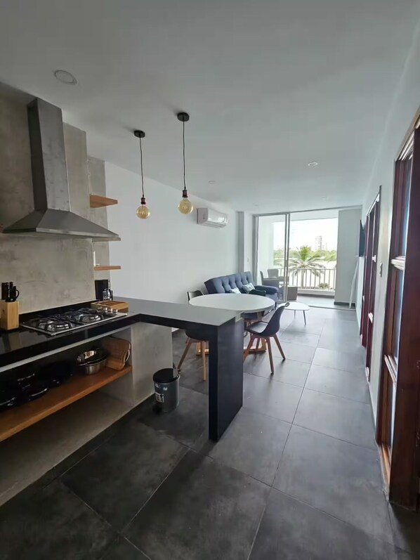 Cocina moderna con isla central, zona de comedor con mesa redonda y sillas, y vistas al exterior a través de grandes ventanales.