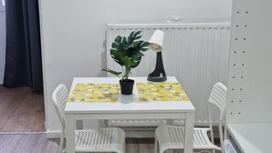 Une petite pièce propre, avec une table blanche, deux chaises, une plante en pot et un radiateur.