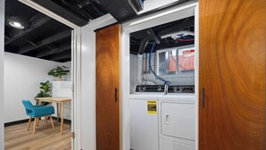 Ett kompakt kök med tvättmaskin, en trädörr och en liten matplats med en blå stol och ett bord.