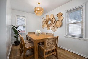 A dining area with a wooden table and chairs, a hanging light fixture, and a wall-mounted woven art piece.