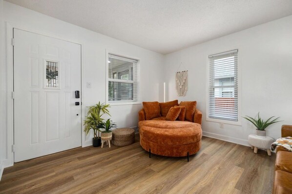 A room with a wooden floor, a white door, a brown sofa, and two windows with blinds.