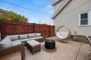 A backyard with a wicker sofa set, a round wicker chair, and a black trash can.