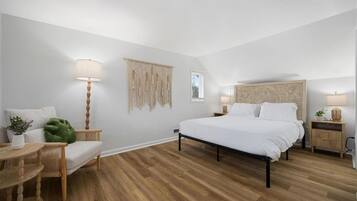 A bedroom with a bed, bedside tables, a lamp, a macrame wall hanging, and a green plant.