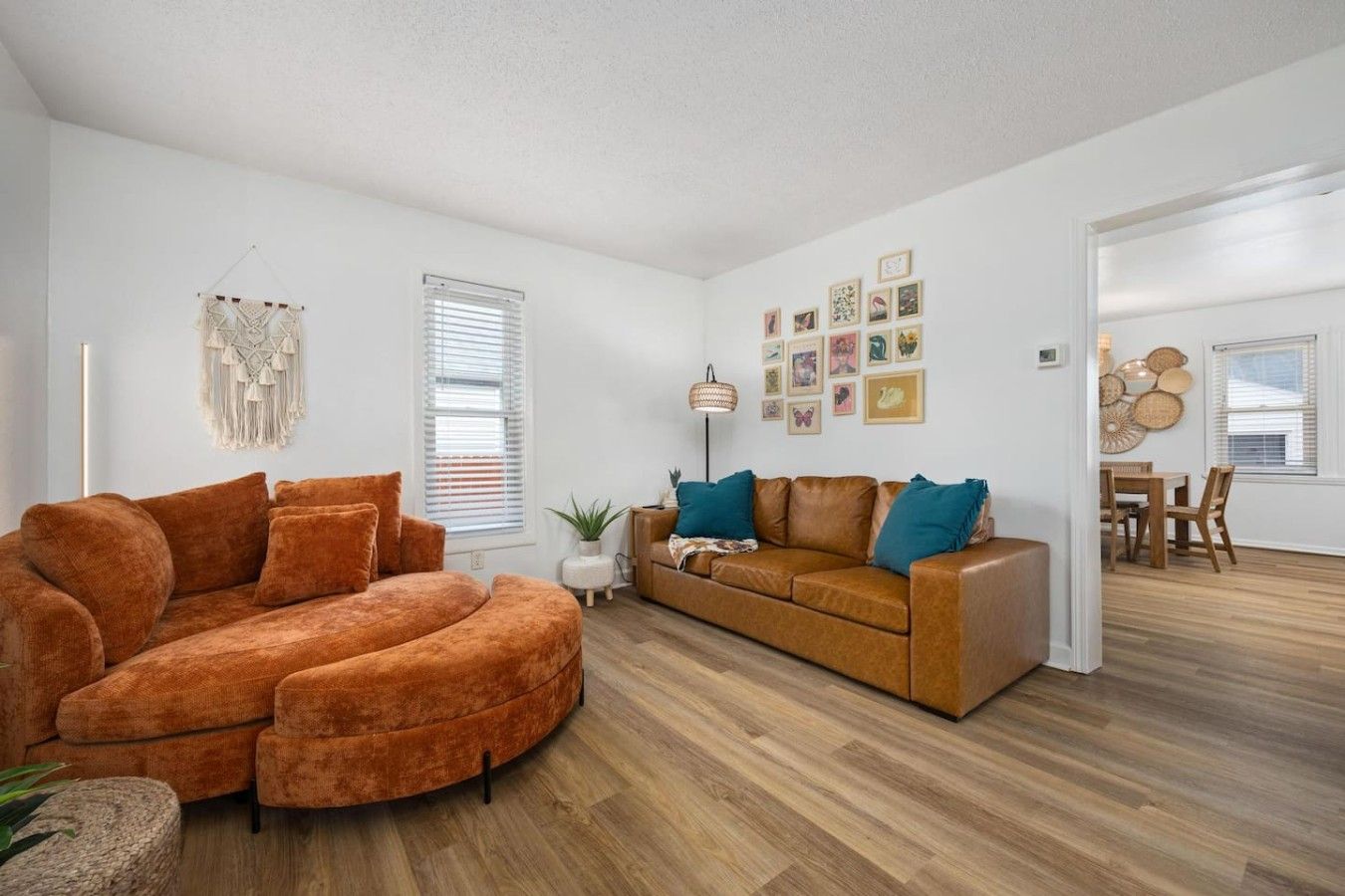 Un salon spacieux avec un grand canapé orange, un fauteuil orange plus petit, un canapé marron agrémenté de coussins turquoise, et un coin repas avec une table et des chaises en bois.