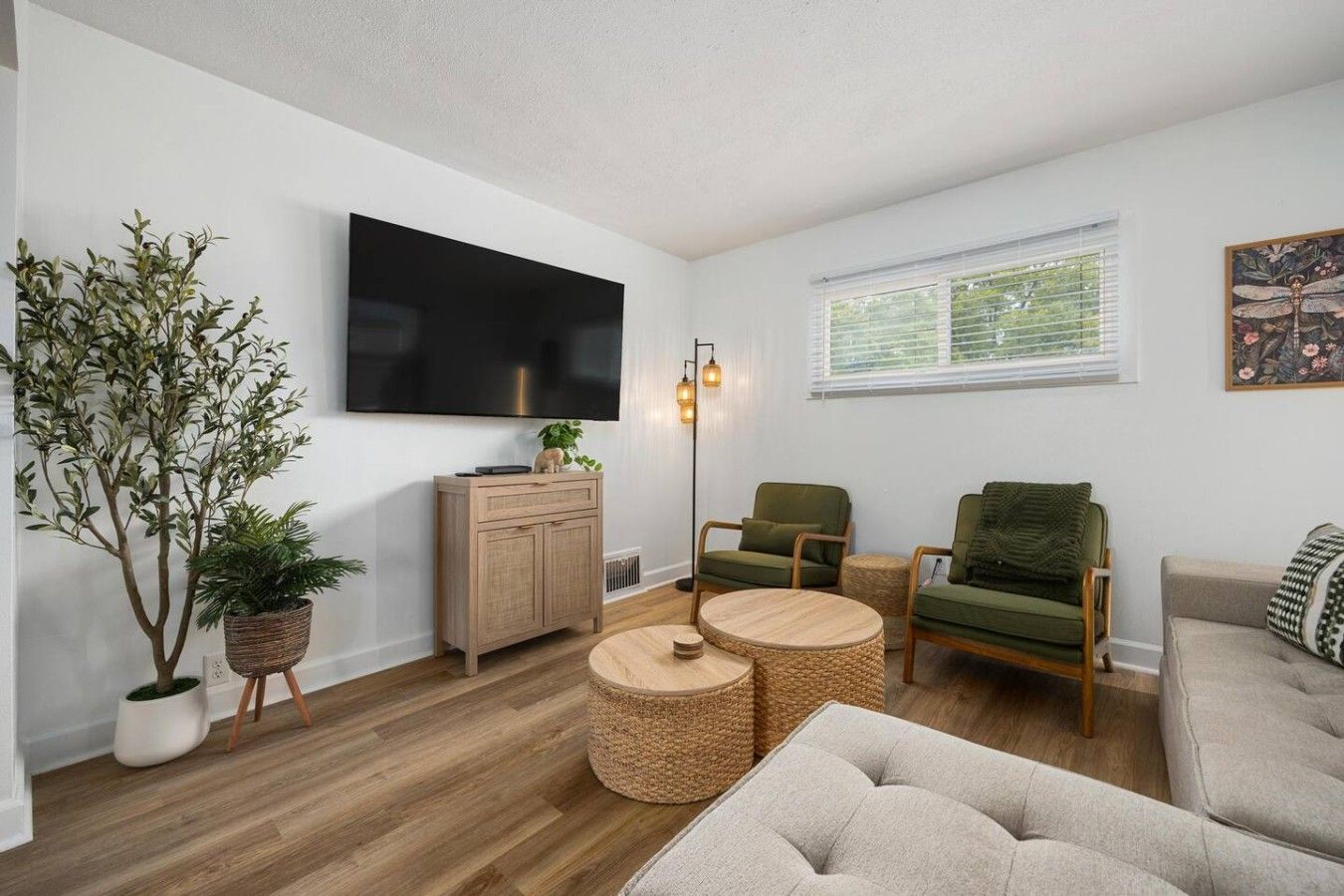 A living room with a flat-screen TV, a wooden cabinet, a green armchair, a round coffee table, and a sofa.
