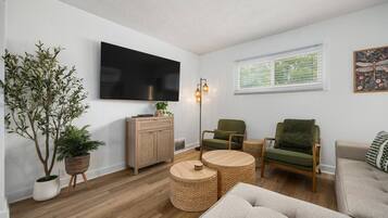 A living room with a flat-screen TV, a wooden cabinet, a green armchair, a round coffee table, and a sofa.