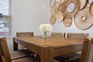 A dining area with a wooden table surrounded by wicker chairs, a vase with white flowers, and woven wall decorations. - Family Retreat, Walk to Prospect Rd at Heights Haus (Peoria Heights)