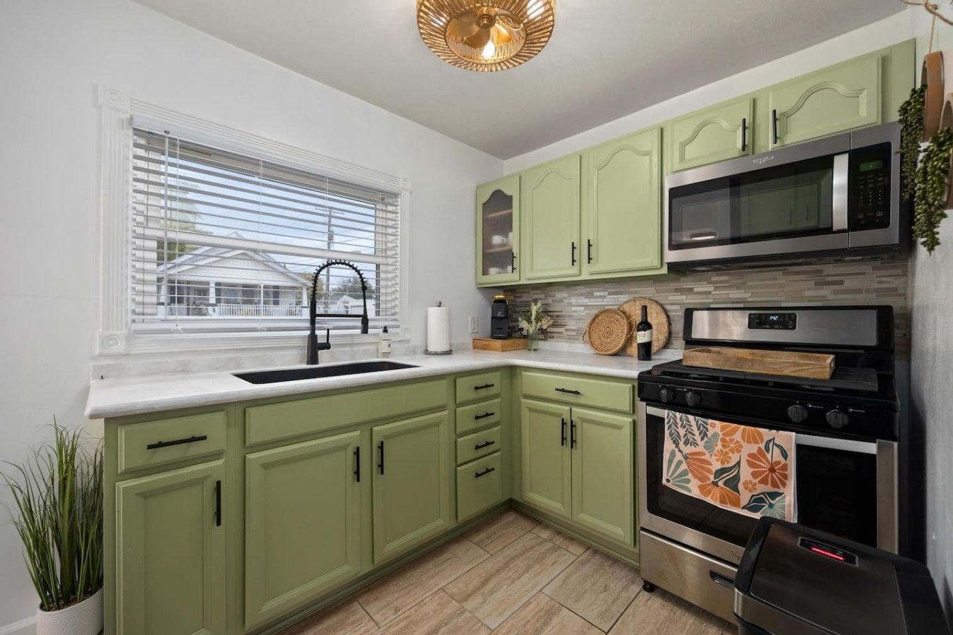 A kitchen with green cabinets, a stainless steel microwave, and a stove.