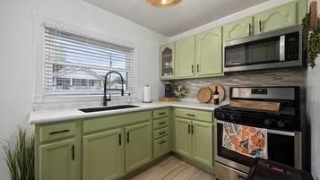 A kitchen with green cabinets, a stainless steel microwave, and a stove.