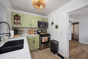 A kitchen with green cabinets, a microwave, an oven, a sink, and a trash can. - Family Retreat, Walk to Prospect Rd at Heights Haus (Peoria Heights)