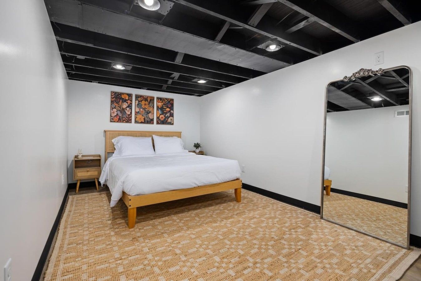 A bedroom with a bed, a nightstand, a mirror, and floral artwork on the wall.