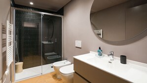 Ein modernes Badezimmer mit Duschkabine aus Glas, einer weißen Toilette, einem Waschbecken inklusive Spiegel und einem Handtuchhalter.
