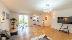 A modern living room with a grey sofa, a TV, and a dining area with a table and chairs. - EXQUIS 2BR Artistic Apartment TAO I Garden I Panzer Kaserne I Parking I Familly (Holzgerlingen)
