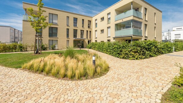 A modern building with a flat roof, rectangular windows, and a paved courtyard with a small tree and grass. - EXQUIS 2BR Artistic Apartment TAO I Garden I Panzer Kaserne I Parking I Familly (Holzgerlingen)