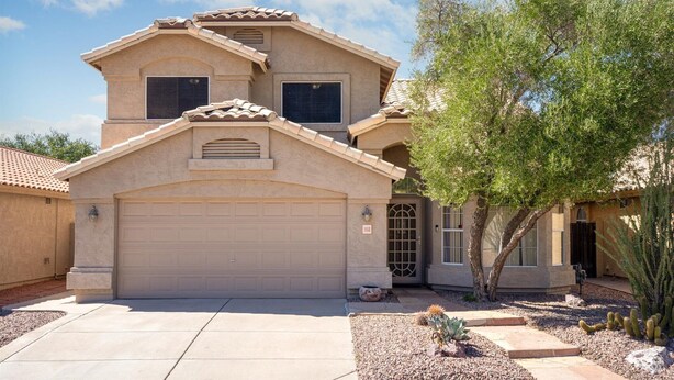 A two-story house with a beige facade, a garage, and a landscaped front yard with cacti and a tree. - Sleeps 10 - Sparkling Pool - 7 mins to DT Chandler (Chandler)