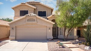 Une maison à deux étages avec une façade beige, un garage et un jardin aménagé avec des cactus et un arbre.