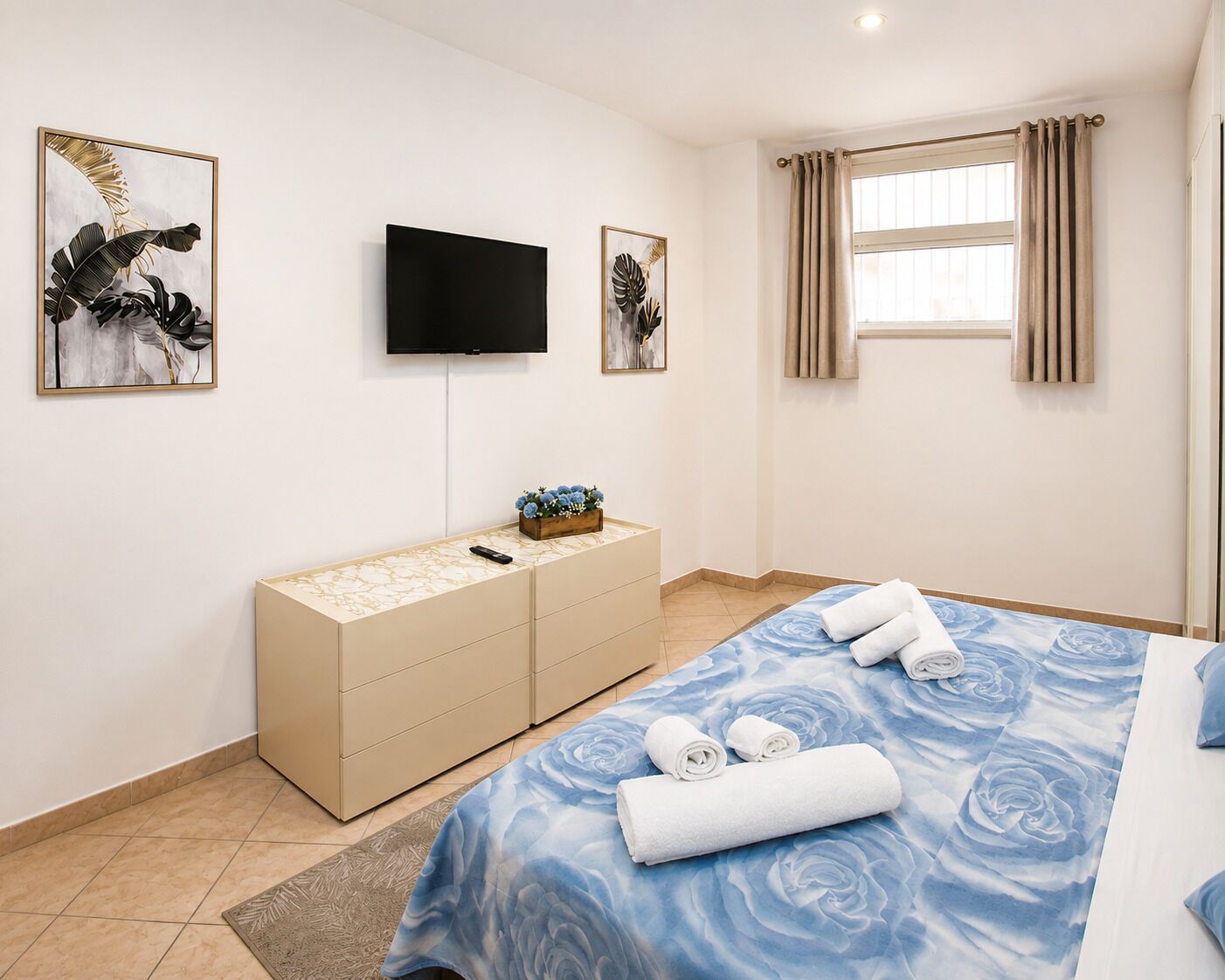 Quarto de hotel com cama, televisão, cômoda e obras de arte nas paredes.